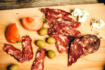 chopped dried sausage and meat with olives and tomato on a wooden board close-up