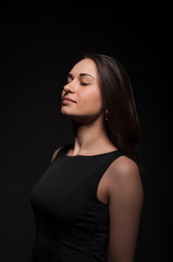 Fototapeta premium Gentle young satisfied lady with closed eyes in the darkness. Elegant black dress, so dark everywhere. Amazing girl with attractive appearance