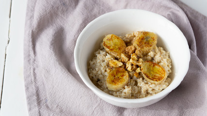 Oatmeal porridge in a bowl with baked bananas, and nuts. Healthy vegetarian breakfast. Top view, copy space. 