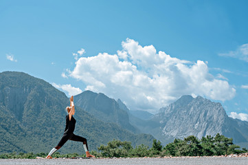 Woman doing yoga poses outside and beautiful view of mountains and sky with clouds