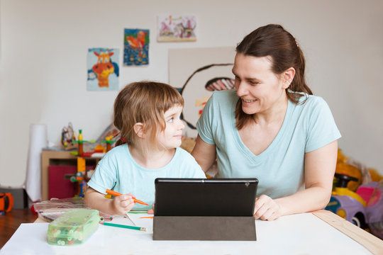Little girl draws paints  with her mother And watches a drawing lesson online on a tablet at home. The concept of distance learning online school. 