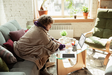 Checking graphs. Man working from home during coronavirus or COVID-19 quarantine, remote office concept. Young businessman, manager doing tasks with smartphone, laptop, tablet has online conference.