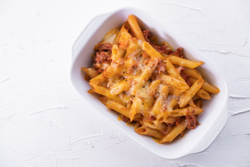 Macaroni bolognesa in baking dish with minced meat, tomato sauce and grated cheese isolated on textured white background Italian cuisine. Top view.