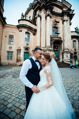 The bride and groom walk together in the park. Charming bride in a white dress, the groom is dressed in a dark elegant suit.