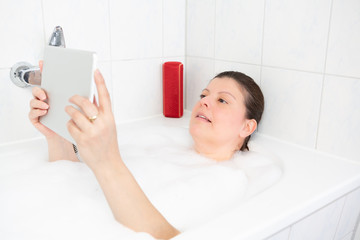 Obraz na płótnie Canvas Lady works from her bathtub, She is using her digital tablet while taking a bubble bath.