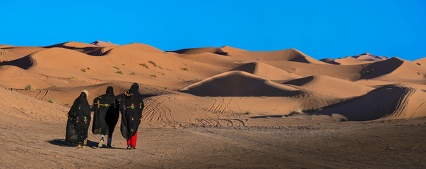 Fototapeta premium Drei Frauen gehen über die Sanddünen in Erg Chebbi Marokko, Panorama 
