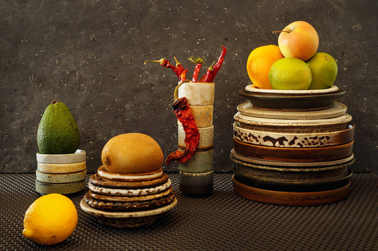 Fresh fruit: orange, lime, Apple, kiwi, avocado on ceramic plates. Hot, dried pepper on saucers made up of a stack and lemon on a textured background. Still-life..