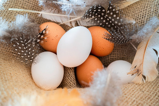 different coloured eggs with feathers lying on a jute bag