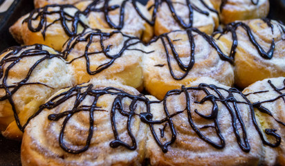 Cinnabon. Cinnamon rolls decorated with chocolate on a stove tray.
