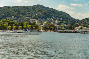Fototapeta premium Como, ITALY - August 4, 2019: Apartments, villas, hotels on the green forested mountainsides near Lake Como. Beautiful Italian Como city. Warm sunny summer day in very popular holiday destination