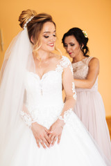bride's girlfriend prepares the bride for her wedding day. The bride's girlfriend helps secure the bride's wedding dress before the ceremony
