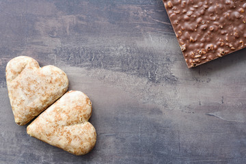 Top view of chocolate bar with nut filling and two gingerbread hearts. Sweets on marble table background. Copy space.