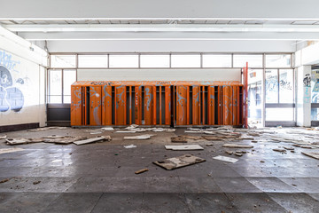 Row of bright orange lockers inside a decaying abandoned school with graffiti