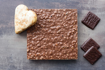 Top view of different types of chocolates and gingerbread heart. Chocolate bar with nut filling. Sweets on marble table background.