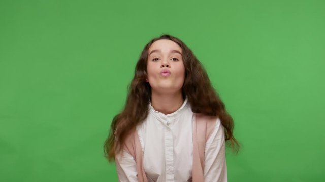 Funny cute teenage brunette girl in white shirt making fish face with pout lips, having fun fooling around with goofy expression, childish carefree mood. studio shot isolated on green background