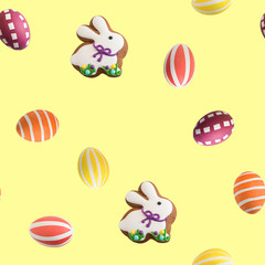 Attributes of the chrestian Easter holiday on a yellow background: multicolored painted eggs and Easter gingerbread in the form of a rabbit