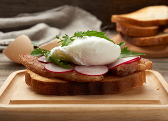 sandwich on toasted white slice of bread with poached eggs, green leaves of arugula and radish