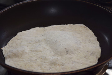 raw dough with spices in the shape of a circle in a hot pan for home baking flat bread