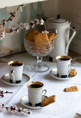 Coffee served with shortbread cookies and sweets on the background of flowering branches and an old cupboard.