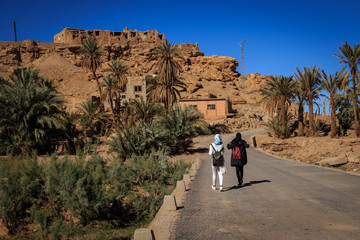 Zwei muslimische Mädchen aus Marokko mit Rucksäcke  gehen auf der Strasse hinauf ins Dorf