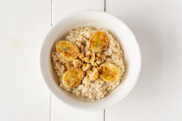 Oatmeal porridge in a bowl with baked bananas, honey and nuts. Healthy vegetarian or vegan breakfast. Copy space, top view. 