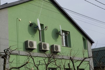 facade of a private house with a green wall with air conditioning windows and satellite dishes against a gray sky