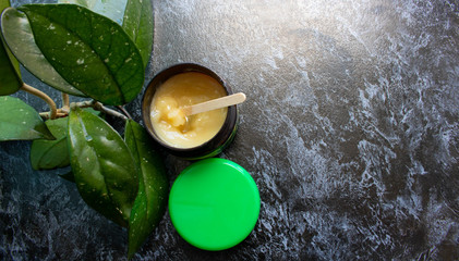 Multi-purpose cream in a small, beautiful, reusable glass container with a green lid on a black surface.