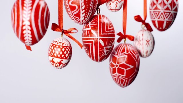 Easter red eggs with white folk pattern, hang from top on red ribbons with bow on white background. Ukrainian traditional eggs pisanka and krashan.