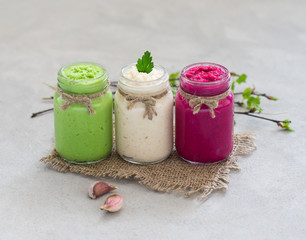 Russian appetizer horseradish with beetroot, green horseradish wasabi, white horseradish with lemon and garlic in jars on a linen napkin on a light gray background