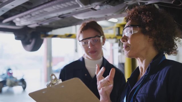 Female tutor and student looking underneath car on hydraulic ramp on auto mechanic course - shot in slow motion 