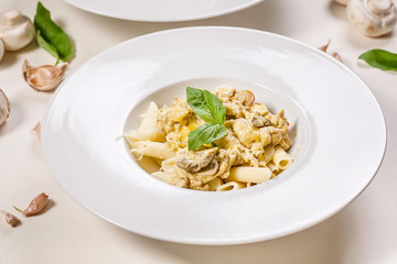 Close-up penne pasta in large white plates with spinach leaves and garlic on a light background. Mediterranean traditional food