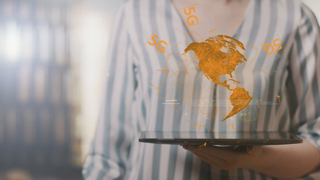 Unrecognizable woman working on a futuristic tablet with a hologram earth and text 5G. Hologram screen. IOT, mobile network, connection and communication technology concept.