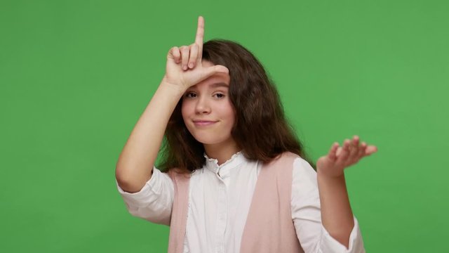 Unhappy depressed teenage brunette girl in white shirt showing loser gesture, L sign on her forehead, disappointed with bad result, upset over defeat. indoor studio shot isolated on green background