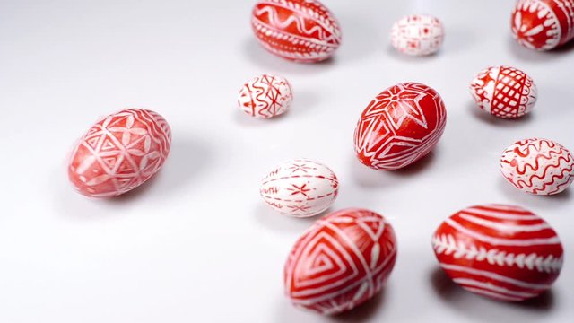 Red easter eggs with folk Ukrainian pattern lay around on white background. And man rotate one egg beside. Ukrainian traditional eggs pisanka and krashanka.