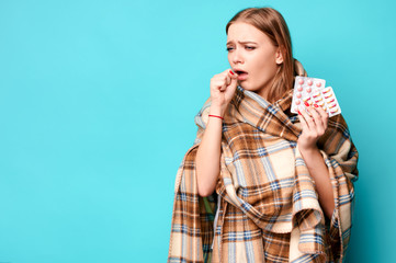 Female with infection holds pills in her hands wrapped in a plaid. Blue background