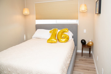 Bed with a white blanket and number 16 in golden balloons 