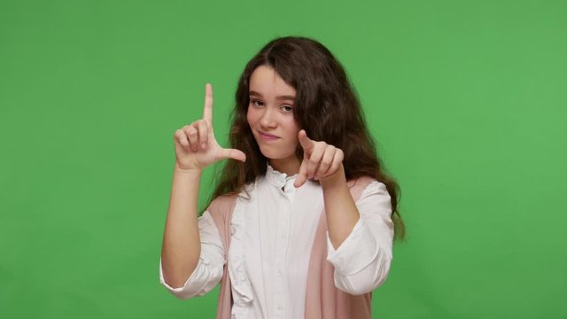 You lose! Teenage brunette girl in white shirt showing loser or lame gesture and pointing to camera, accusing you of defeat, mocking failure, unsuccess. indoor studio shot isolated on green background