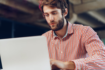 Portrait of young caucasian businessman using laptop computer at his workplace in modern office
