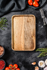 Wooden cutting board  in center of Fresh raw greens, vegetables. Healthy, clean eating, vegan, dieting food concept. Black background. Top view. Copy space