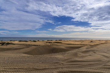 Fototapeta na wymiar People passing through sand dunes overlooking the ocean on the horizon during a sunny day with thick clouds moving in the sky from the Grand Canary Island