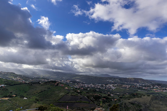 Rock volcanic formation and surrounding nature, capturing trees and shrubs moving in strong wind during a sunny afternoon with a blue sky in the valley area of the Gran Canary Island