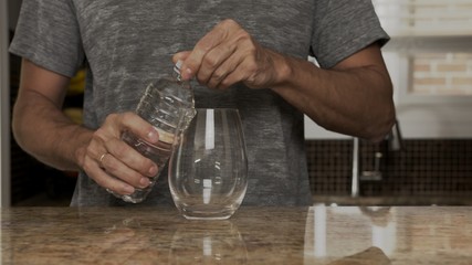 Young man in a gray T-shirt pours water into a glass from a stainless steel thermos or plastic bottle in a beautiful fashionable kitchen. healthy lifestyle. Handsome man is thirsty.