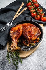 Baked chicken leg with seasonings in a frying pan. Gray background. Top view