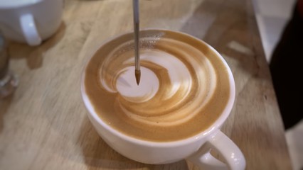 cup of coffee with milk and latte art making tool