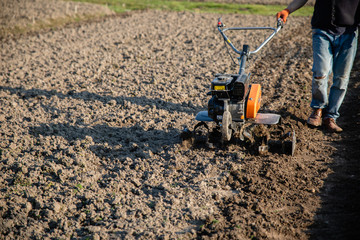 Fototapeta premium small plowing machine in hands of a farmer making arable in black soil