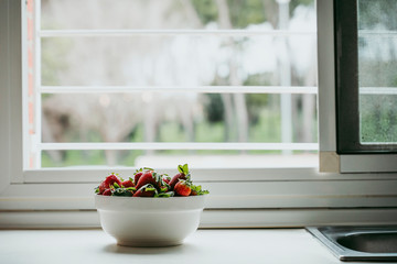 Strawberries in white bowl with a window behind.