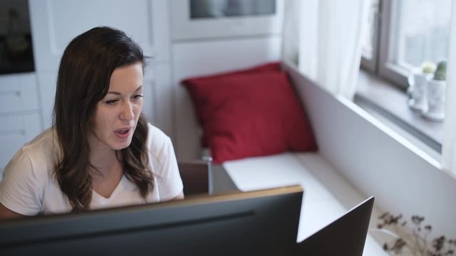A young, beautiful woman is looking at a computer monitor. Remote work. Online teaching. The teacher shows the exercise. The neuropsychologist works remotely. Home furnishings.
