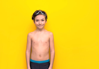 Boy swimmer with glasses on his head and in swimming trunks on a yellow background. Smiling 9 years old boy in swimming trunks. Summer season, sea and relaxation at sea, in the pool