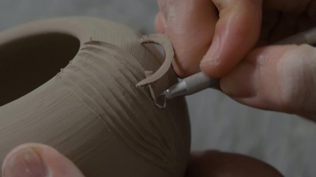 The Potter begins forming a pattern on a clay vase. The first cut on the vase. The chips are nicely separated. Close-up