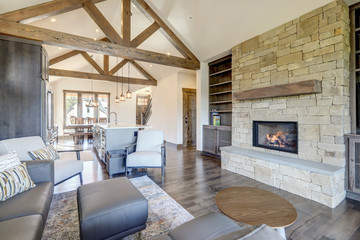 Beautiful large bright vaulted ceiling with large wooden beams and white walls living room interior with stone and leather sofa and dark grey hardwood.